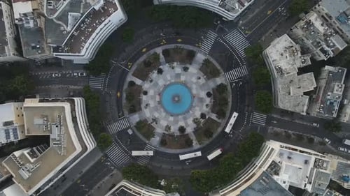 Aerial Lockdown Shot Of Vehicles Moving On Road At Roundabout In City, Drone Flying Over Structures