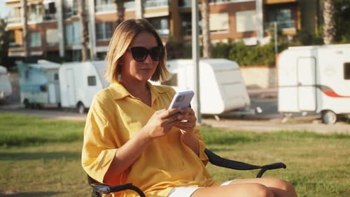 Woman Using Smartphone Sitting Outdoors in Chair