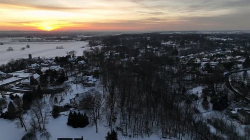 Snowy winter landscape with leafless trees, snow-covered farm fields and houses in American suburb.