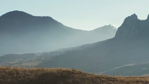 Man Running Across Grassy Hillside in Mountains