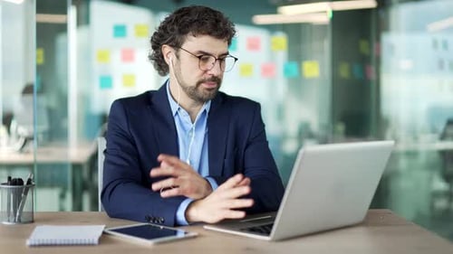 Confident businessman talking on a video call using a laptop sitting at workplace in office. A man
