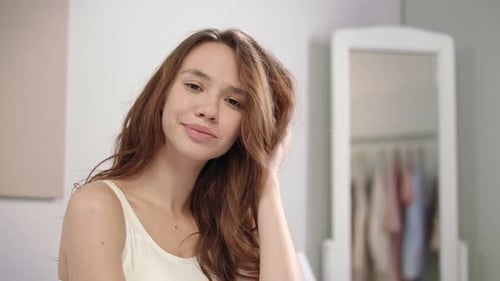 Smiling woman in tank top flips long brown hair