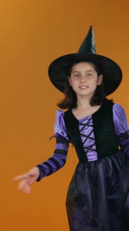 Girl in Witch Outfit Appearing from Corner and Waving on Orange Backdrop