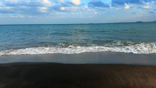 Olas del mar rompiendo en una playa de arena oscura bajo un cielo nublado. Paisaje costero con arena oscura