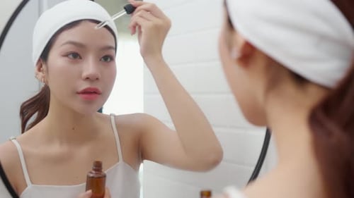Woman Applying Facial Serum in Bathroom Mirror