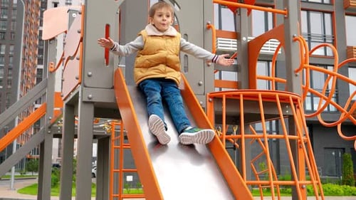 Extreme slow motion of happy cheerful boy riding down on slide at playground