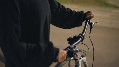 Unidentifiable person holding handlebars on bicycle at night