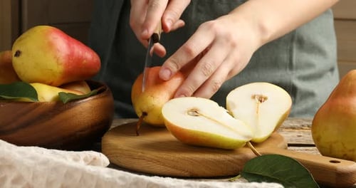 Woman cutting fresh pears at wooden table, closeup