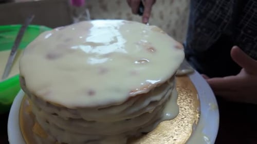 The process of applying the final layer of frosting to the cake. Top view of a kitchen table with to