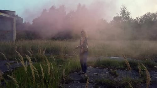 Woman Walking in Field with Pink Smoke at Dusk