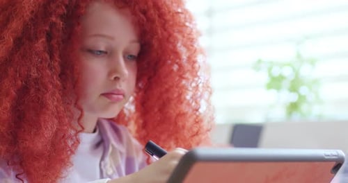 Close Up of Clever Schoolgirl with Red Curly Hair Sitting in Classroom and Using Tablet Device at