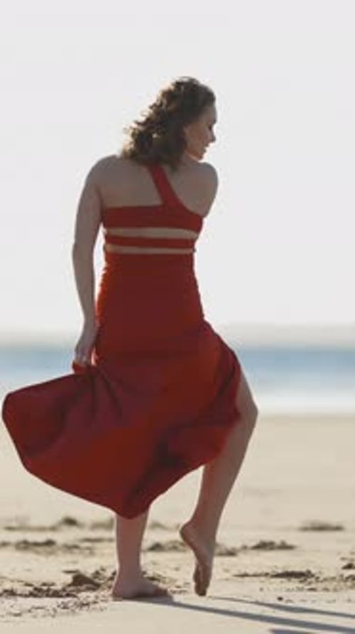 Graceful Young Woman in Red Dress Dancing on the Beach