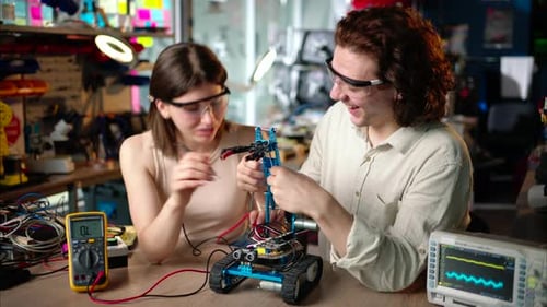 Two young happy engineers fixing a mechanical robot car in the workshop, using VR virtual reality he