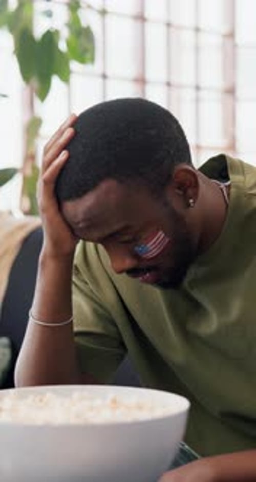 Disappointment, soccer game or black man on sofa with American flag, snacks