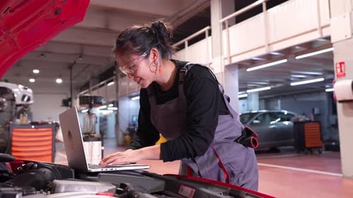 Female Mechanic Running Diagnostics on Car Engine Using Laptop