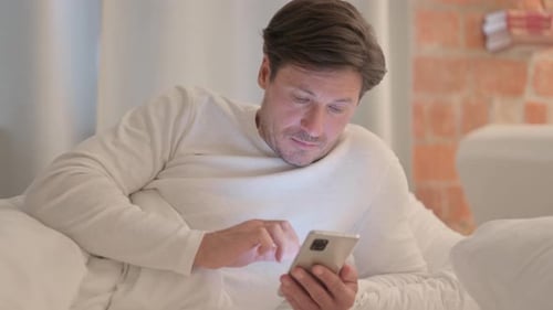 Man Lies in Bed Using Smartphone Device