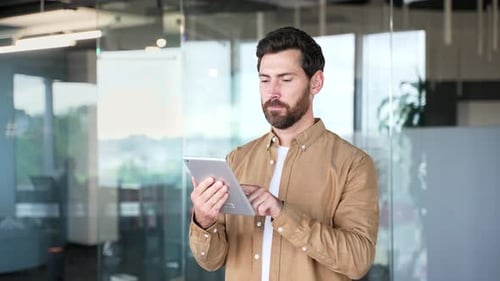 Businessman is using digital tablet standing in modern business office. Handsome bearded manager