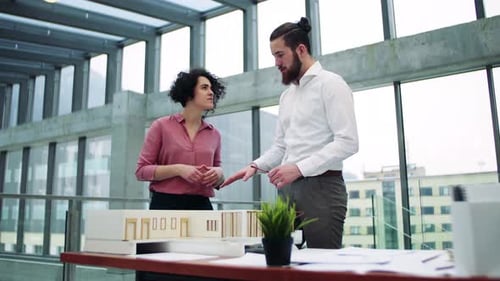Young Architects with Model of a House Standing in Office, Talking