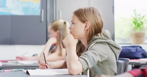 Diverse schoolchildren writing and sitting at desks in school classroom