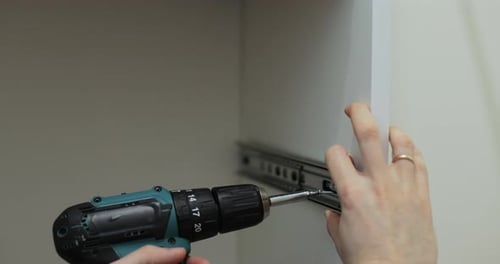 Man Using a Electric Drill to Attach a Metal Drawer Slide to a Piece of Furniture During Assembly