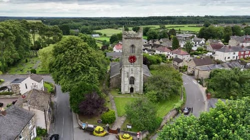 Aerial drone footage captures historic clock tower standing tall amid lush green trees during daytim