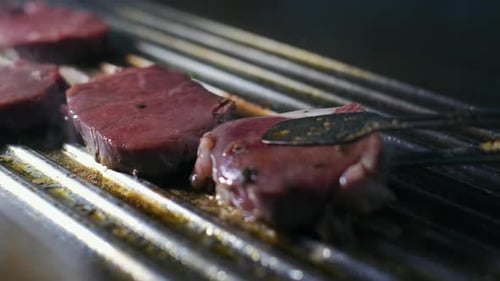 Chef preparing a delicious meal. Cooker frying pieces of juicy beef meat on grill. Steak grilled on