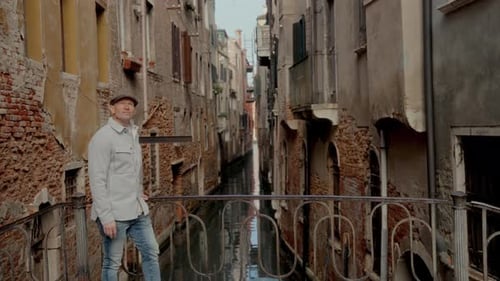 Man In Jacket And Hat Crosses Small Bridge Near A Canal In Venice