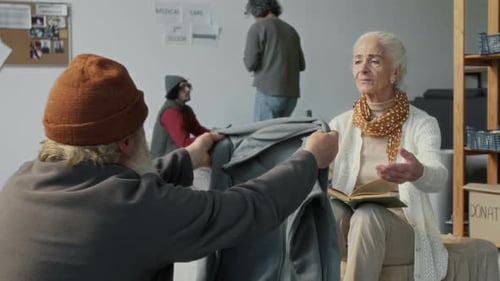 Elderly Man Sharing Warm Clothes with Senior Woman in Refugee Shelter