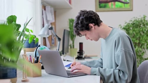 Young Male College Student Sitting at Desk at Home Using Laptop