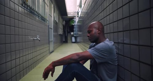 Afroamerikanischer Mann sitzt alleine auf dem Boden in einem engen Korridor, stille Verzweiflung, emotional