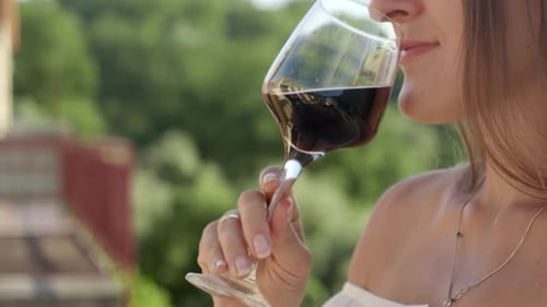 Elegant brunette woman drink red wine from a glass on the balcony or villa terrace