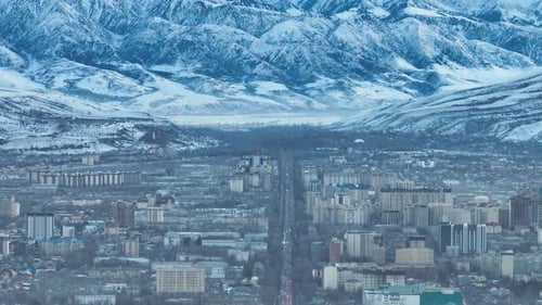 El horizonte de la ciudad bañado por una luz dorada contra enormes montañas cubiertas de nieve