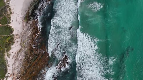Turquoise ocean waves wash up on empty rugged Cape Town beach - aerial top down
