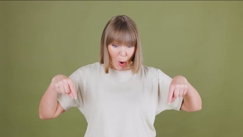 Senior Woman Smiling and Pointing Downwards in a Neutraltoned Studio Space During a Lighthearted