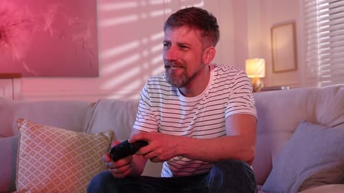 Glücklicher Mann mit Controller spielt zu Hause Videospiel auf dem Sofa