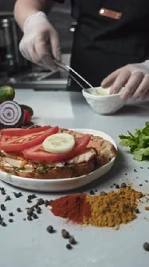 Chef of an Expensive Restaurant in the Kitchen Adds Cucumbers to a Sandwich with Tongs