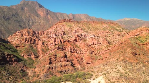 Aerial view drone flying over scenic red rocky mountains with a clear blue sky.