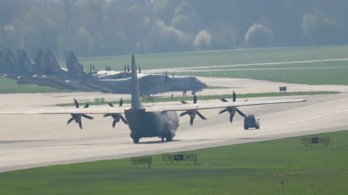 C-130 Hercules takes off in brilliant sunshine at bustling airfield