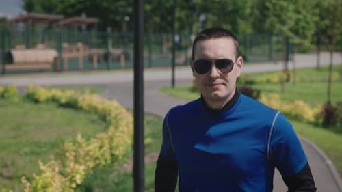 A Successful and Selfconfident Young Man Runs Through a Beautiful and Wellmaintained City Park