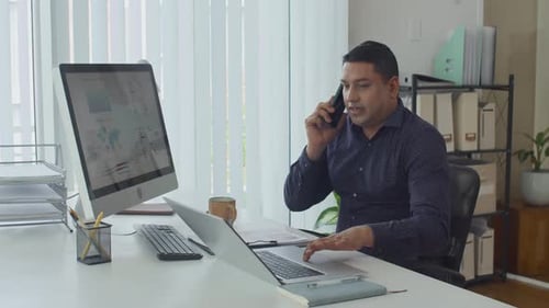 Middle-aged Manager Calling on Phone Working on Computers at Office