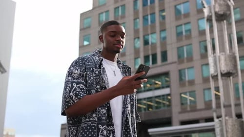 African American Man Checking His Phone While Standing Outside Modern City Buildings