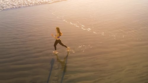 Aerial shot of fit asian woman jogging on the beach at sunset.