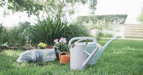 Close up of watering cans, flowers and pots in sunny garden, slow motion