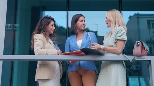 Group of businesswomen standing outside in front of modern office talking.