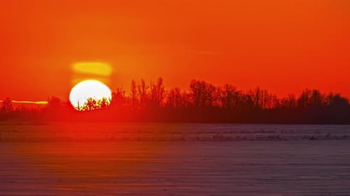 Time-lapse of blinding sun rising in golden sky over snowy landscape. Sky for copy space