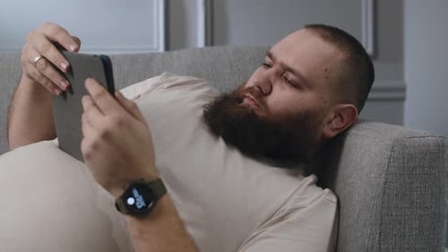 Man Relaxing on Couch Using Tablet