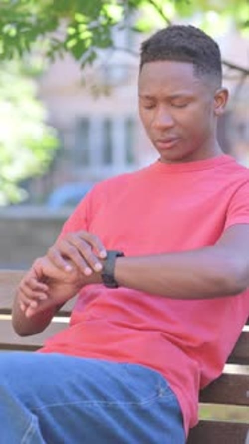 Young Man Checks Time While Sitting on Bench