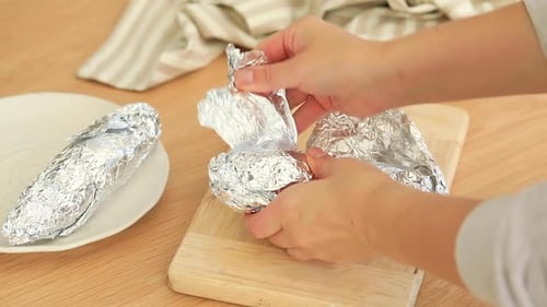 Unwrapping Sweet Potato from Aluminum Foil on Board
