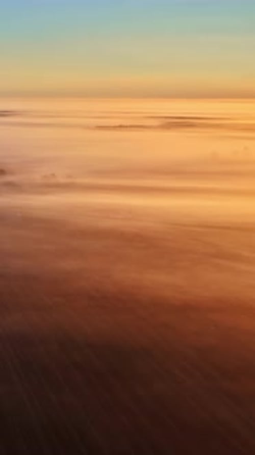 Vue par drone de la couche brumeuse en dessous, se déplaçant lentement dans une lueur dorée brillante