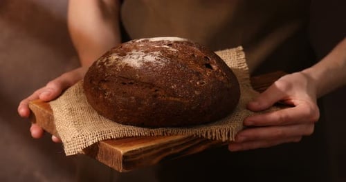 Person Presenting Fresh Baked Bread on Wooden Board